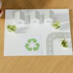 A paper model of a sustainable community featuring houses and recycling symbol, emphasizing eco-friendly living.